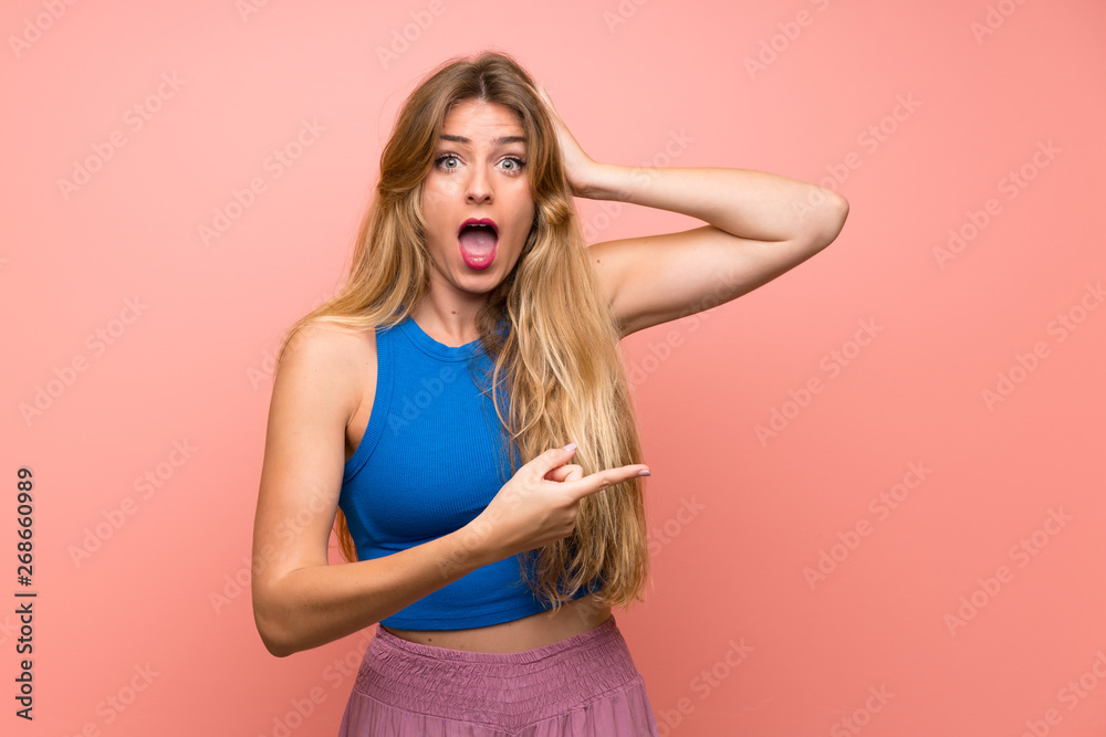 Young blonde woman over isolated pink background surprised and pointing finger to the side Young blonde woman over isolated pink background surprised and pointing finger to the side