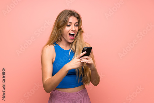 Young blonde woman over isolated pink background surprised and sending a message