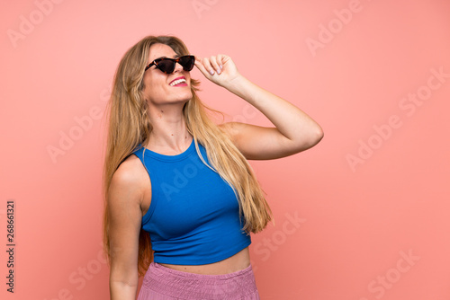 Young blonde woman over isolated pink background with glasses and smiling