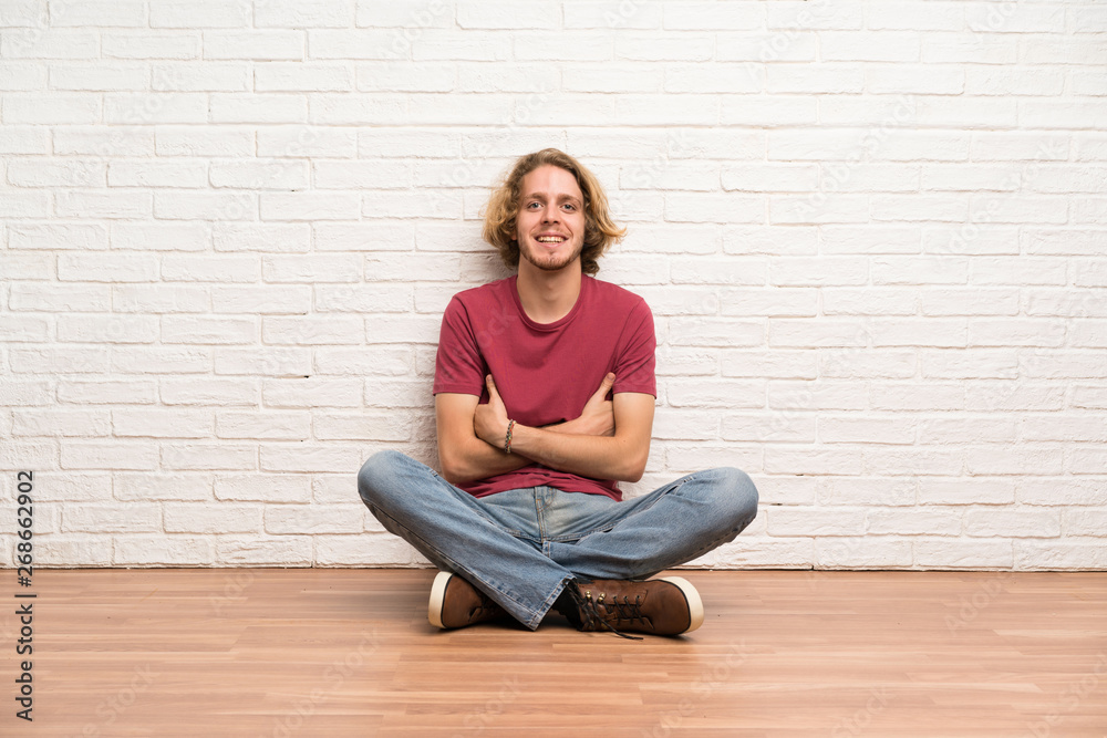 Blonde man sitting on the floor keeping the arms crossed in frontal position Blonde man sitting on the floor keeping the arms crossed in frontal position