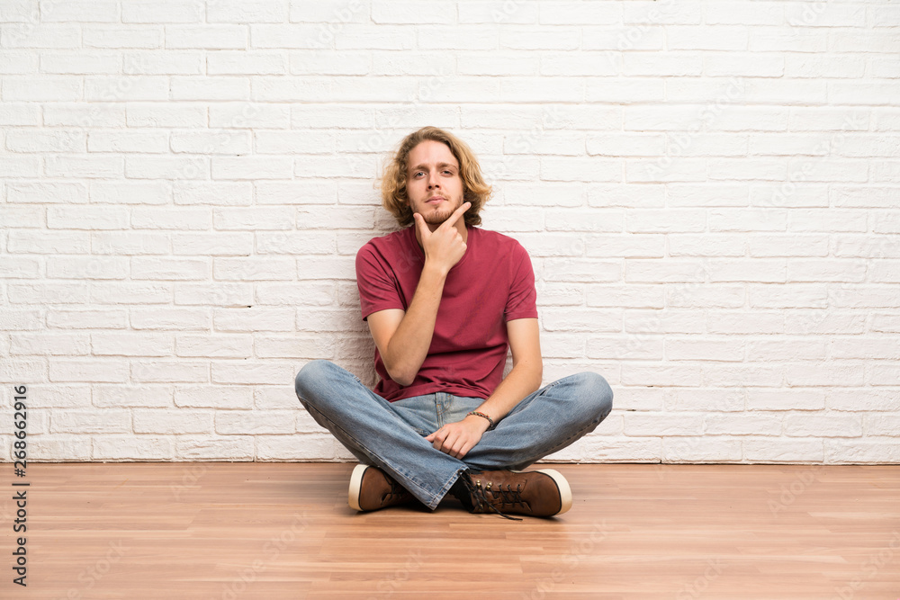 Blonde man sitting on the floor thinking Blonde man sitting on the floor thinking