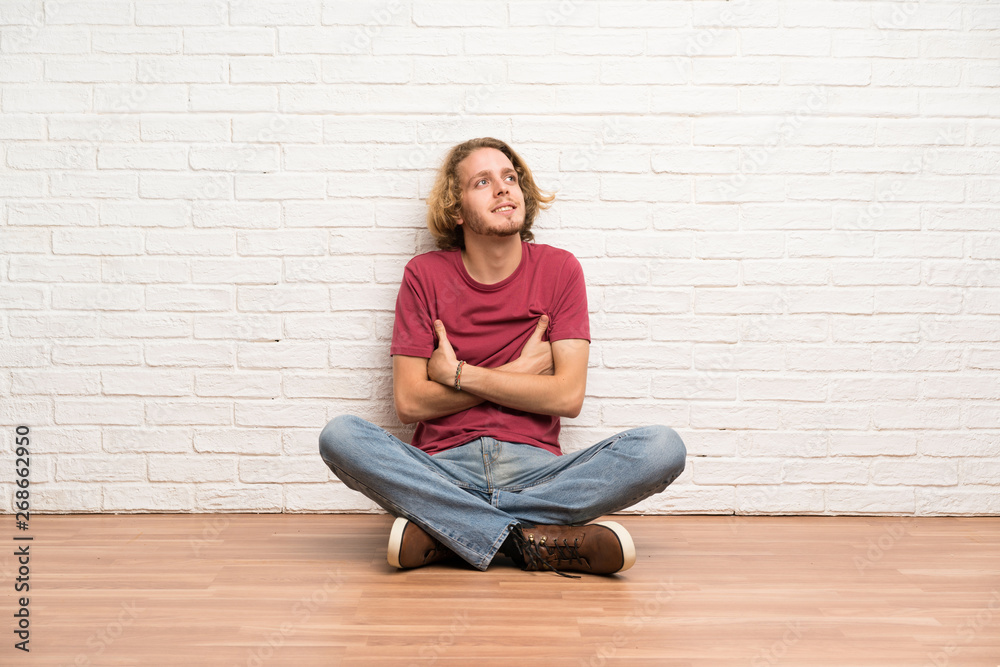 Blonde man sitting on the floor looking up while smiling Blonde man sitting on the floor looking up while smiling