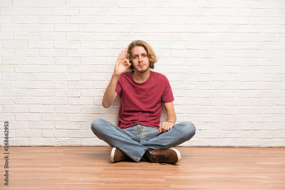 Blonde man sitting on the floor showing ok sign with fingers