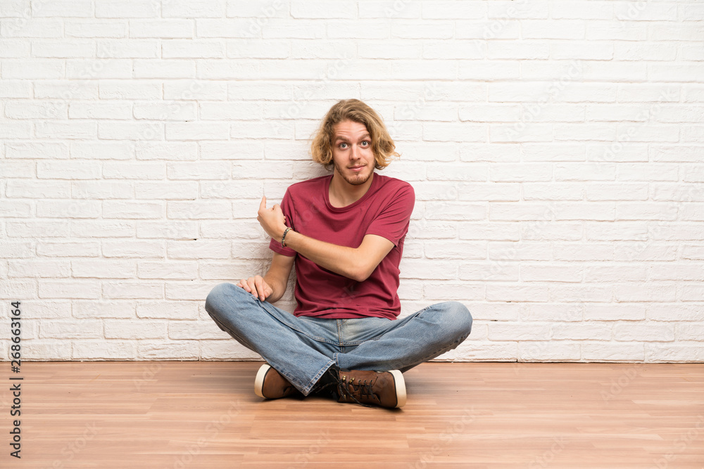 Blonde man sitting on the floor pointing back Blonde man sitting on the floor pointing back