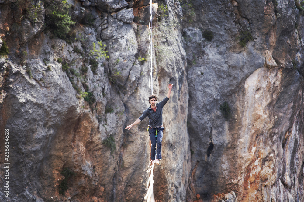 A man is walking along a stretched sling. Highline in the mountains. Man catches balance. Performance of a tightrope walker in nature. Highliner on the background of valley. A man is walking along a stretched sling. Highline in the mountains. Man catches balance. Performance of a tightrope walker in nature. Highliner on the background of valley.