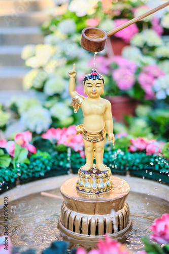 Pouring water over small statue of Buddha surrounded by flowers