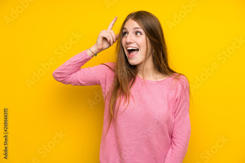 Young woman with long hair over isolated yellow wall intending to realizes the solution while lifting a finger up