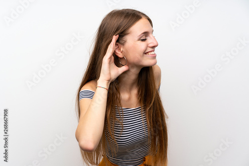 Young woman with long hair over isolated white wall listening to something by putting hand on the ear © luismolinero