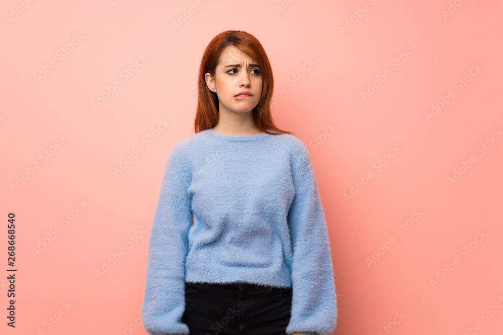 Fototapeta premium Young redhead woman over pink background with confuse face expression while bites lip