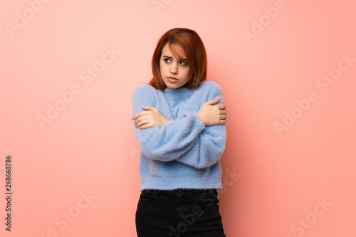 Young redhead woman over pink background freezing