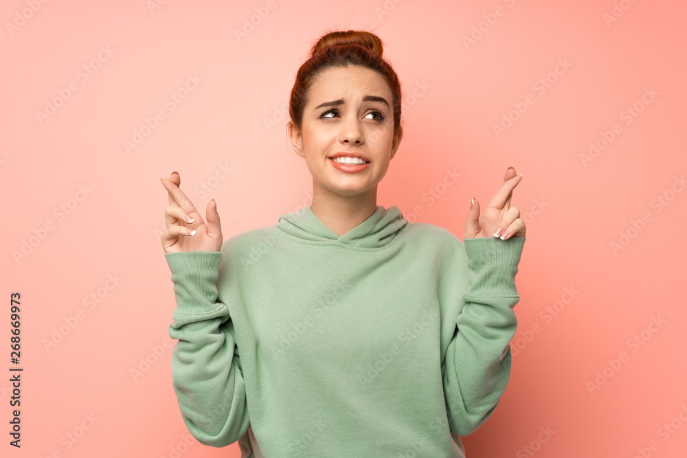 Young redhead woman with sweatshirt with fingers crossing and wishing the best Young redhead woman with sweatshirt with fingers crossing and wishing the best