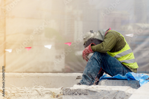 Fototapeta The tired construction worker in the green waistcoat and the red glove sitting i