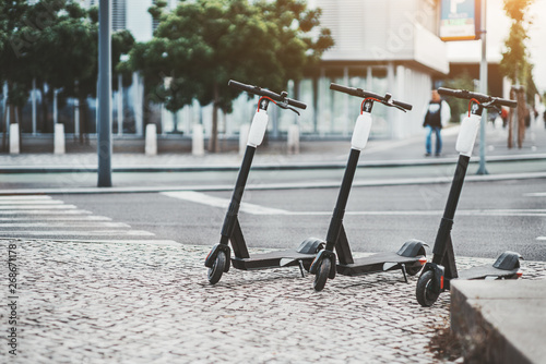 Electric urban transportation: three modern electric readies to ride scooter bikes with accumulators in the center of a city on the pavement stone with the road and crosswalk behind, Lisbon, Portugal