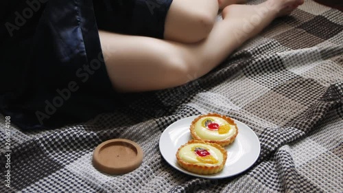 The girl wakes up with morning coffee and cake in bed. Beautiful young woman drinking coffee at home in her bed in a cozy blue robe.