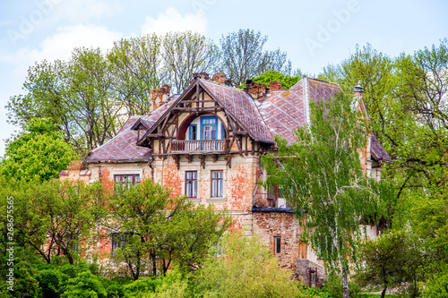 Old house in Gothic style among green trees in sunny weather_
