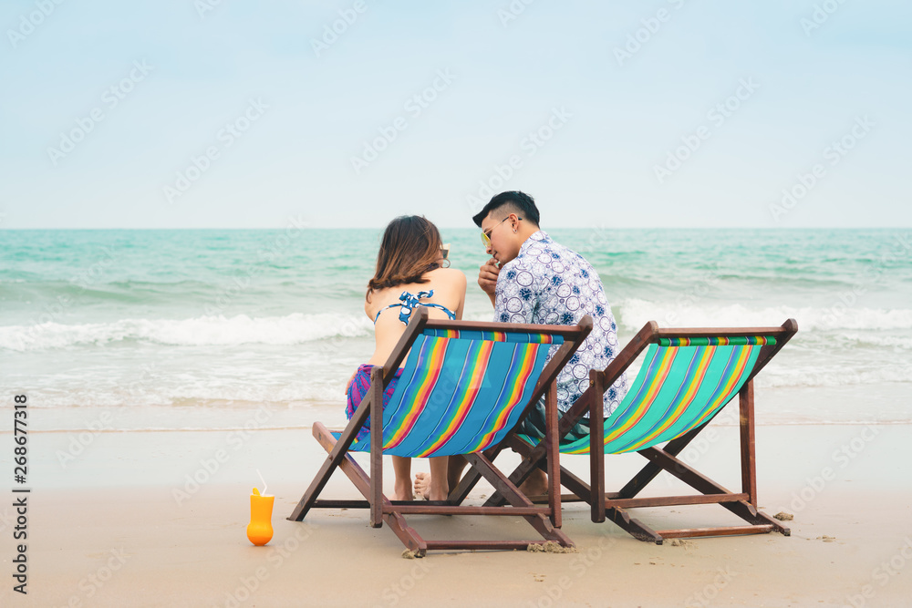 Couple in love sitting on the beach chairs on tropical beach in summer holiday