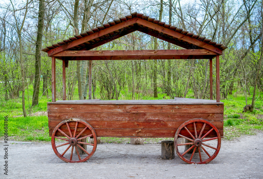 Empty trading stand decorated as an old wooden cart with roof in a park – green grass and trees.