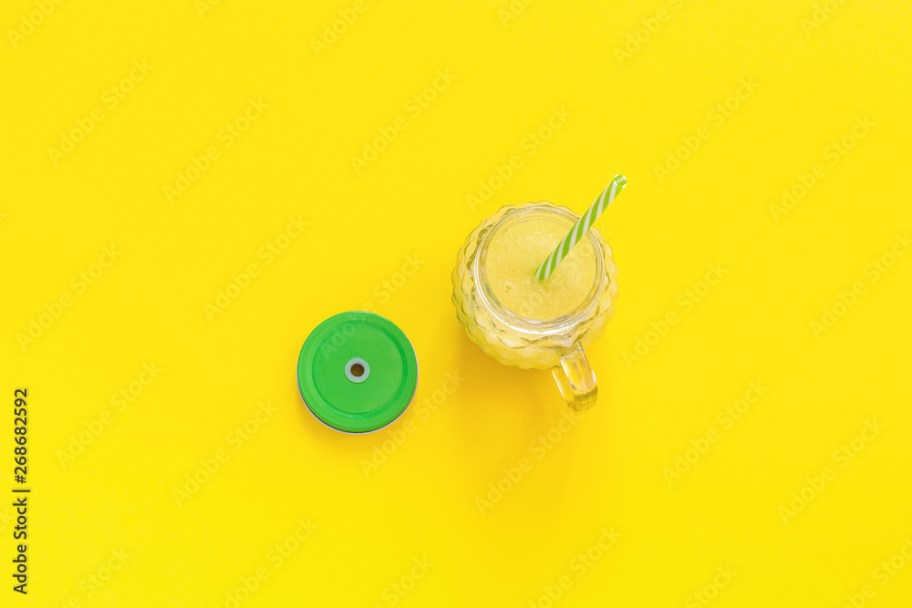 glass jar with natural yellow fruit juice, smoothie or fresh with green lid and cocktail straw on yellow background. Top view Copy space Template