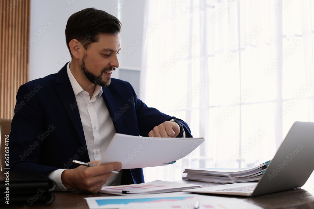 Businessman looking at wristwatch while working with documents in office Businessman looking at wristwatch while working with documents in office