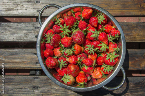 Red and fresh strawberries in an aluminum dish on a wooden table