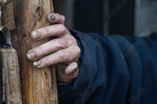 The dirty hand of a very old man with sore fingers and nails rests on a wooden pole on the threshold of the house © Sahaidachnyi Roman
