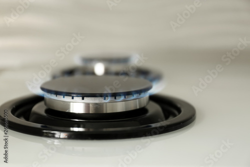 Gas burner with blue flame on modern stove, closeup. Space for text