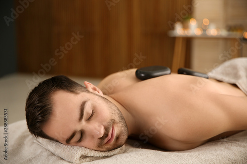 Handsome man receiving hot stone massage in spa salon. Space for text