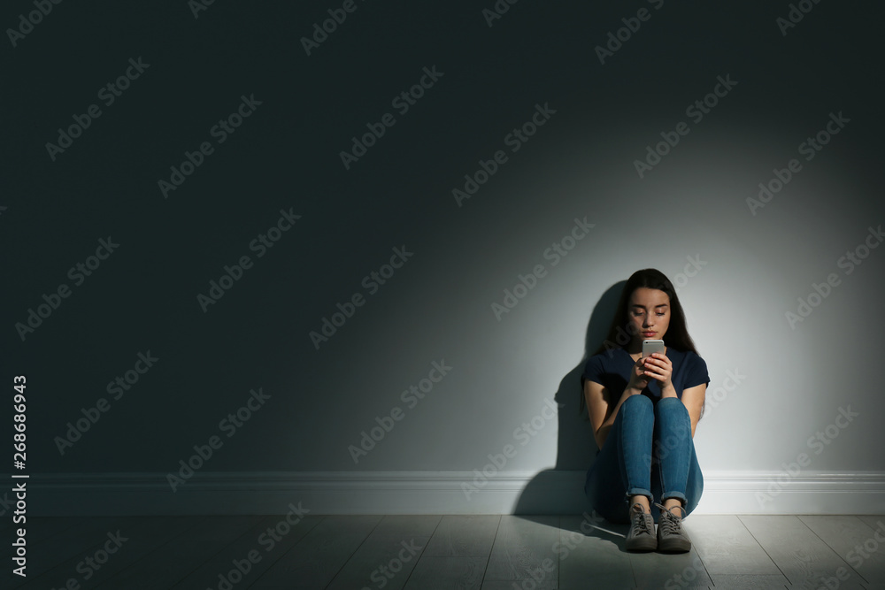 Lonely woman with smart phone sitting on floor in dark room. Space for text - obrazy, fototapety, plakaty 