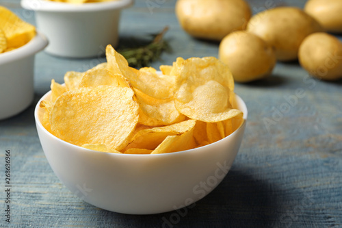 Bowl of crispy potato chips on wooden table