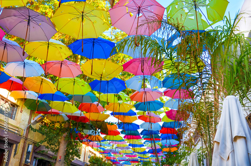 Colorful umbrellas decorating the top of the street in Cypriot Nicosia. The umbrella serves also as a shade and protection against the sunshine. Among the umbrellas there are green tree branches photo