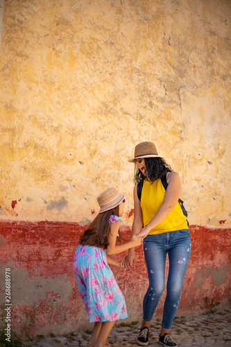 A mother and her daughter is jumping in front of a cracked ( rustic ) wall with happiness