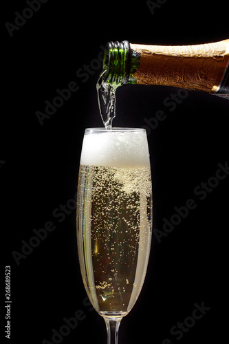 A Close-up of a bottle pouring champagne into a champagne flute on a black background