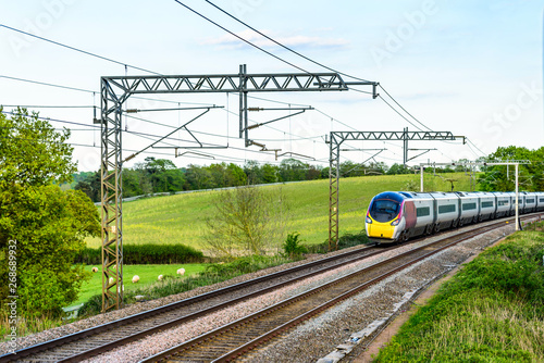 uk train railroad next to rapeseed field in bloom day view in england. spring railway landscape