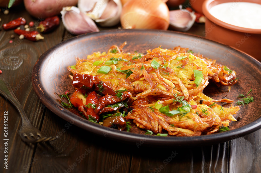 Homemade tasty potato pancakes in clay dish with sun-dried tomatoes and sour cream Homemade tasty potato pancakes in clay dish with sun-dried tomatoes and sour cream
