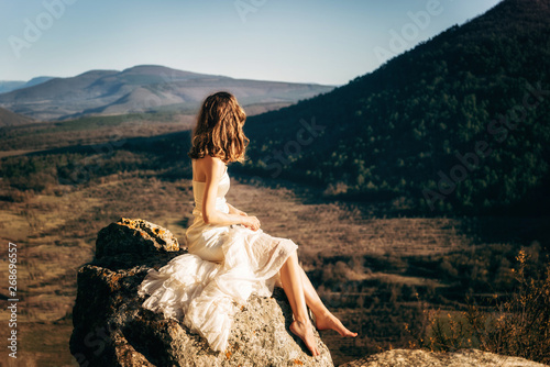 Kachi-Kalon, Bakhchysarai, Republic of Crimea, Russia - April 1, 2019: A girl in a white dress sitting on a stone in the mountains Kachi-Kalyon