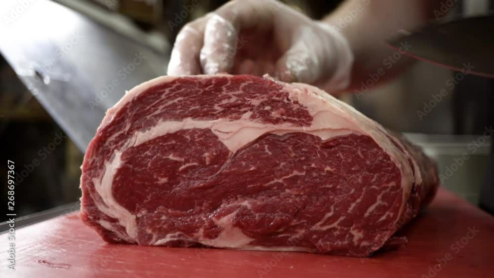 Butcher in gloves cuts carcass of red meat. Action. Close-up of professional knife cutting huge piece of meat in butcher shop