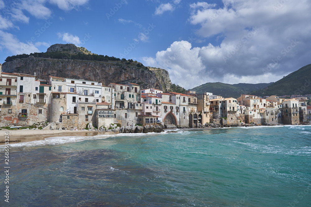 Cityscape Picture of old, ancient and romantic city Cefalu from seaside in italian island Sicily taken in sunny spring day with clouds on sky. Typical example of historic mediterranean architecture.