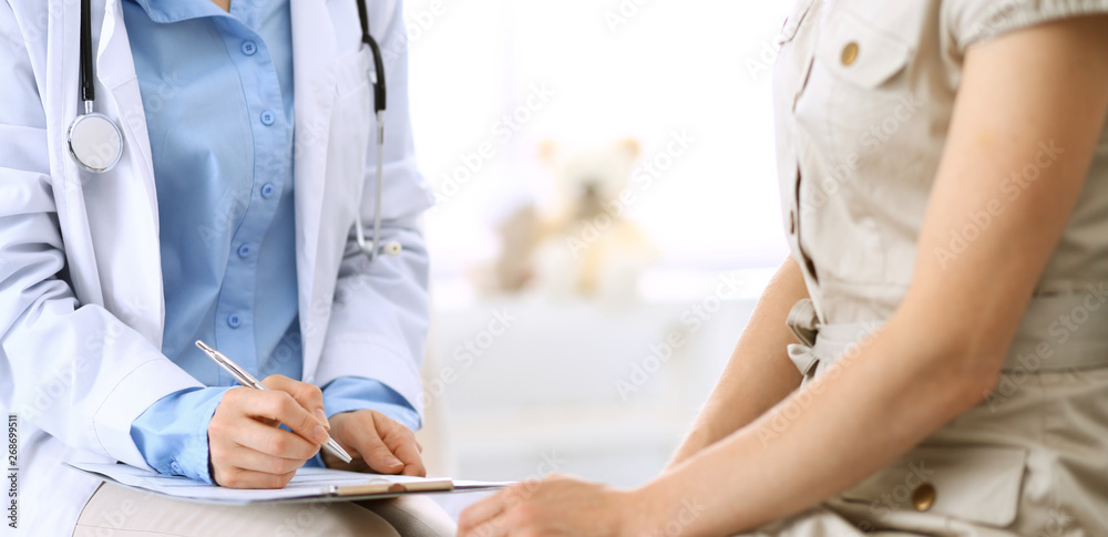 Doctor and patient talking. Physician at work in hospital while writing up medication history records form on clipboard near sitting woman. Healthcare and medicine concepts Doctor and patient talking. Physician at work in hospital while writing up medication history records form on clipboard near sitting woman. Healthcare and medicine concepts