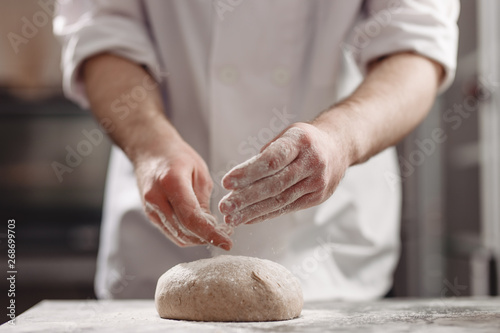 Baker kneads dough on the table in the bakery