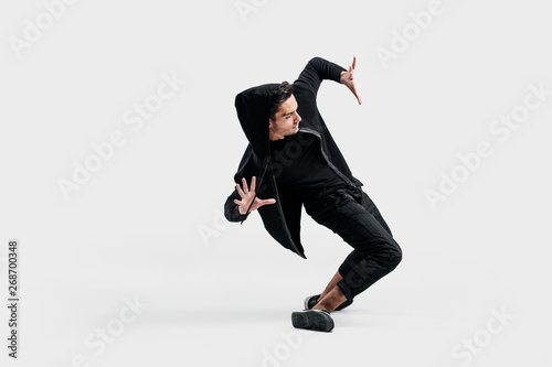 Dark-haired stylish dancer dressed in a black clothes makes stylized movements of street dance