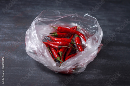 Zero waste shopping concept. Red hot peppers in a plastic bag on a black background. Ban one-time use of plastic.