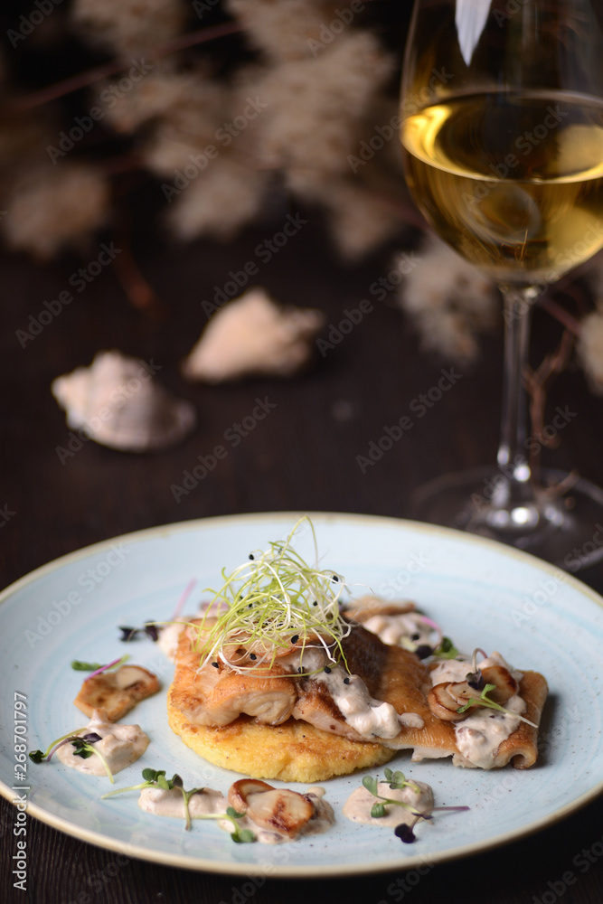 fried fish fillet with a sauce on the background of a glass of wine
