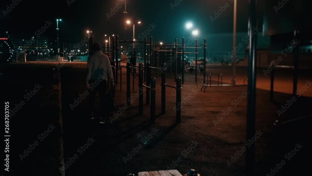 Young man is going out from sports ground in park at night Young man is going out from sports ground in park at night