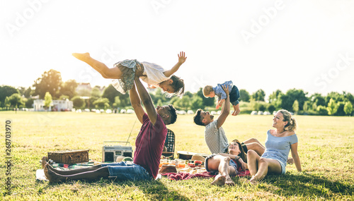 Young multiracial families having fun playing with kids at pic nic barbecue party - Multicultural joy and love concept with mixed race people together with children at park - Warm contrasted filter