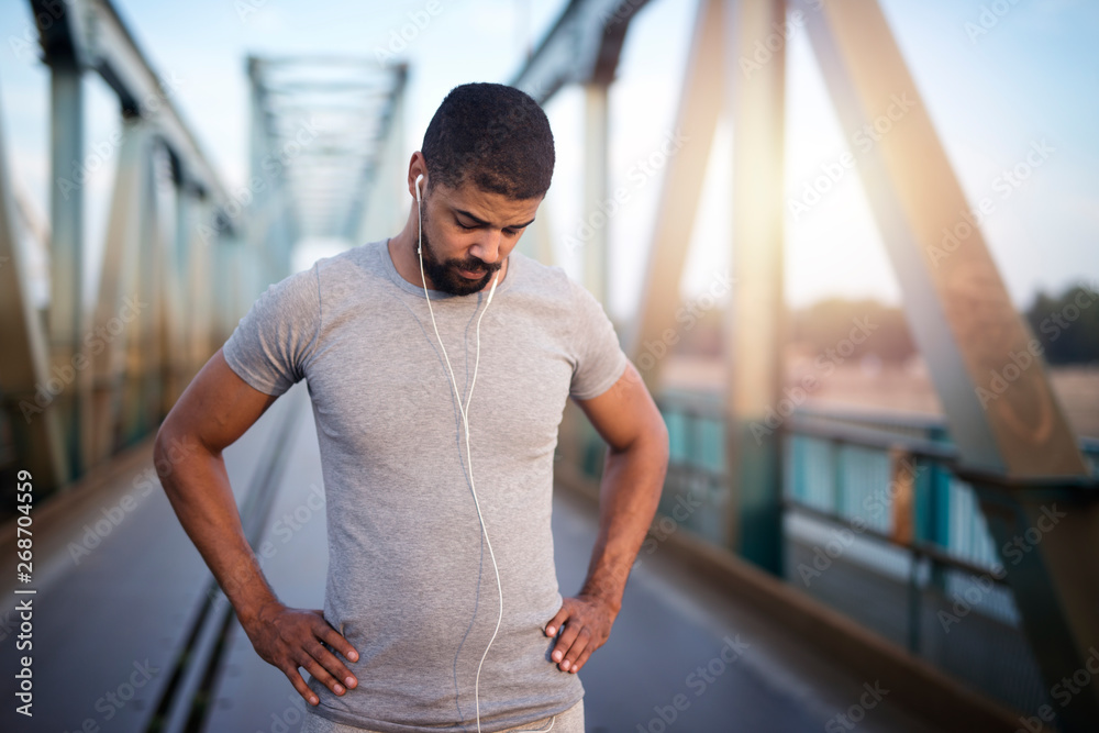 Portrait of handsome athlete with earphones preparing for training. Active and healthy lifestyle. Looking down getting concentrated.