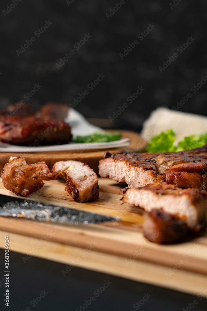 person cutting cooked or grilled beef steak with a knife on a wooden boards