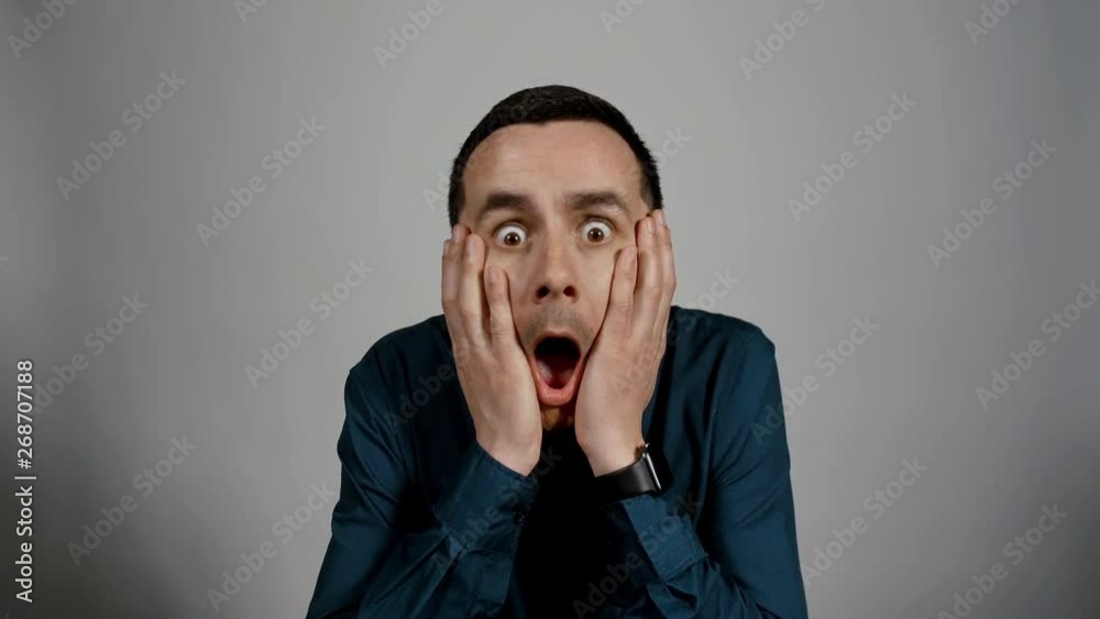 Closeup portrait of a young business man is very surprised and holds his hands against his head looking into the camera on a white background. Charismatic actor play concept of emotions Closeup portrait of a young business man is very surprised and holds his hands against his head looking into the camera on a white background. Charismatic actor play concept of emotions
