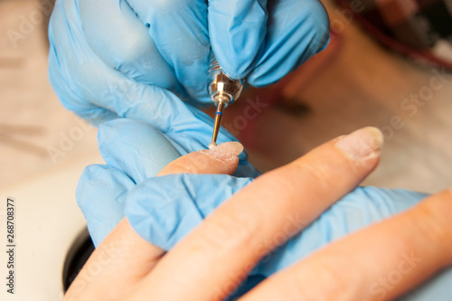 Women's hands - the master in blue gloves makes the client hardware manicure