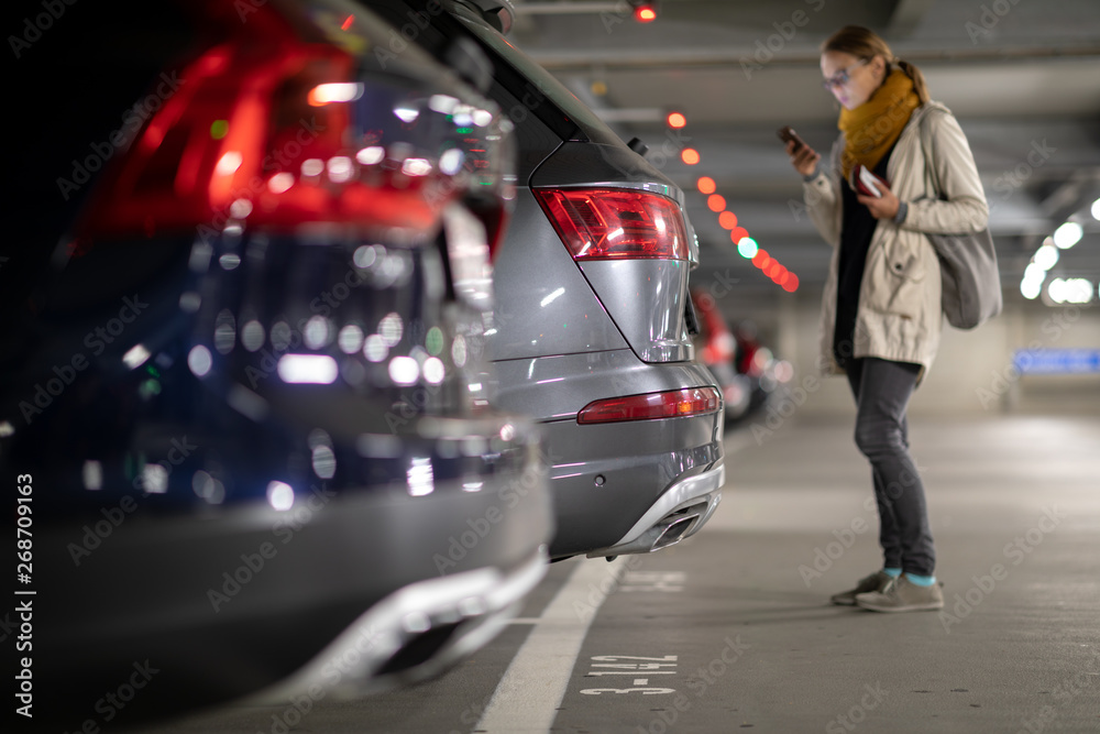 Obraz premium Underground garage or modern car parking with lots of vehicles, perspective of the row of the cars with a female driver looking for her vehicle