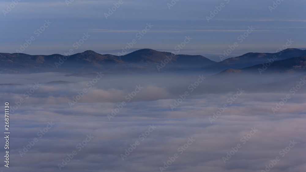 Landscape with inverse cloudiness and protruding peaks of mountains during sunrise.